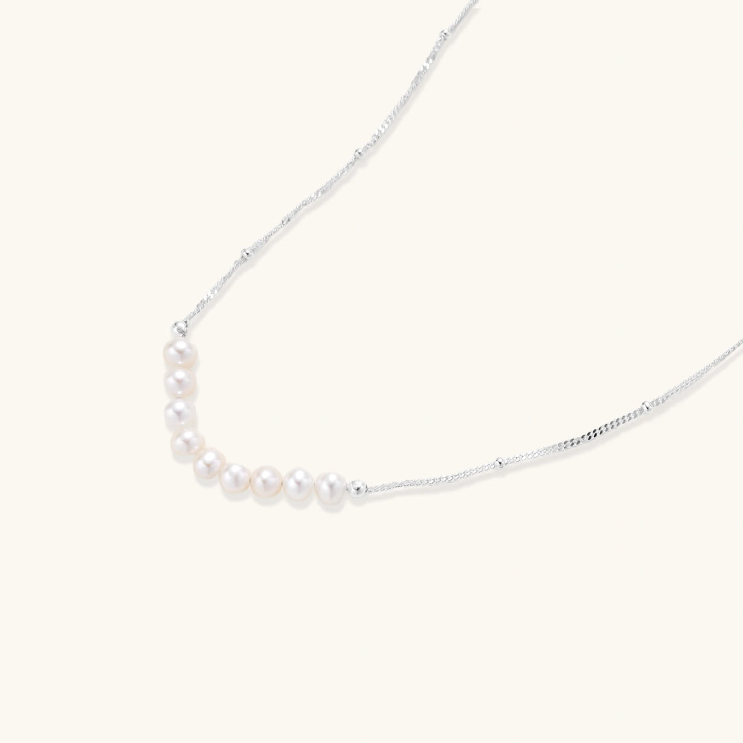 Delicate sterling silver chain necklace with small freshwater pearls arranged in a curved smile arc on cream background.